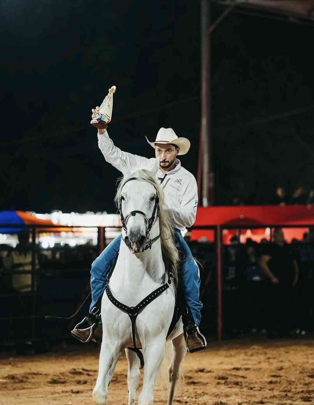 Marco Vinholi a cavalo em rodeio, com chapéu, segurando a imagem de Nossa Senhora Aparecida